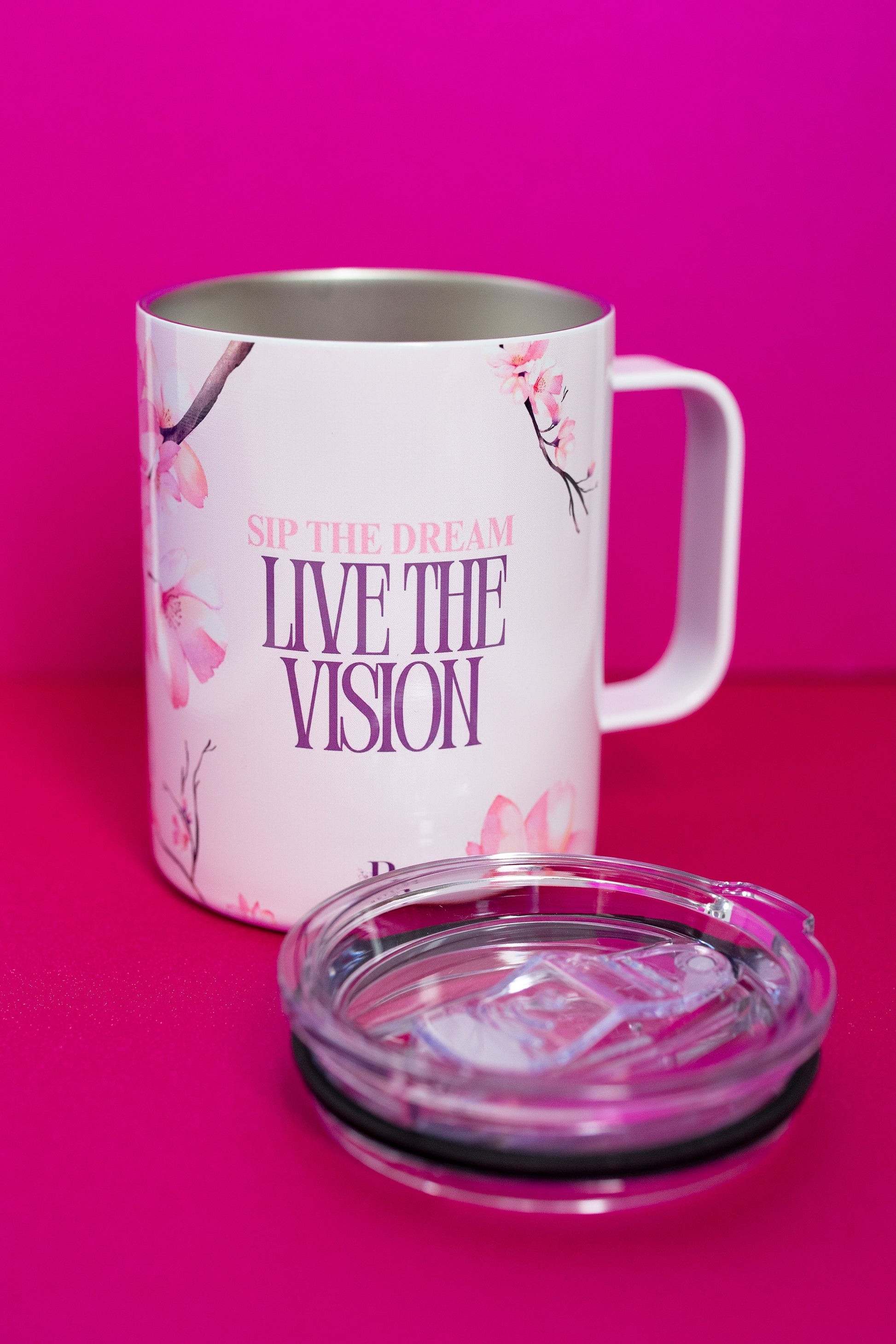 Belivra ceramic mug with the uplifting quote "Sip the Dream, Live the Vision" in purple and pink text, surrounded by delicate cherry blossom illustrations. The mug is displayed with a clear, spill-resistant lid, ideal for enjoying coffee, tea, or your favorite beverages while embracing goals and vision. Perfect for mindful sipping, desk decor, and inspiring morning rituals.