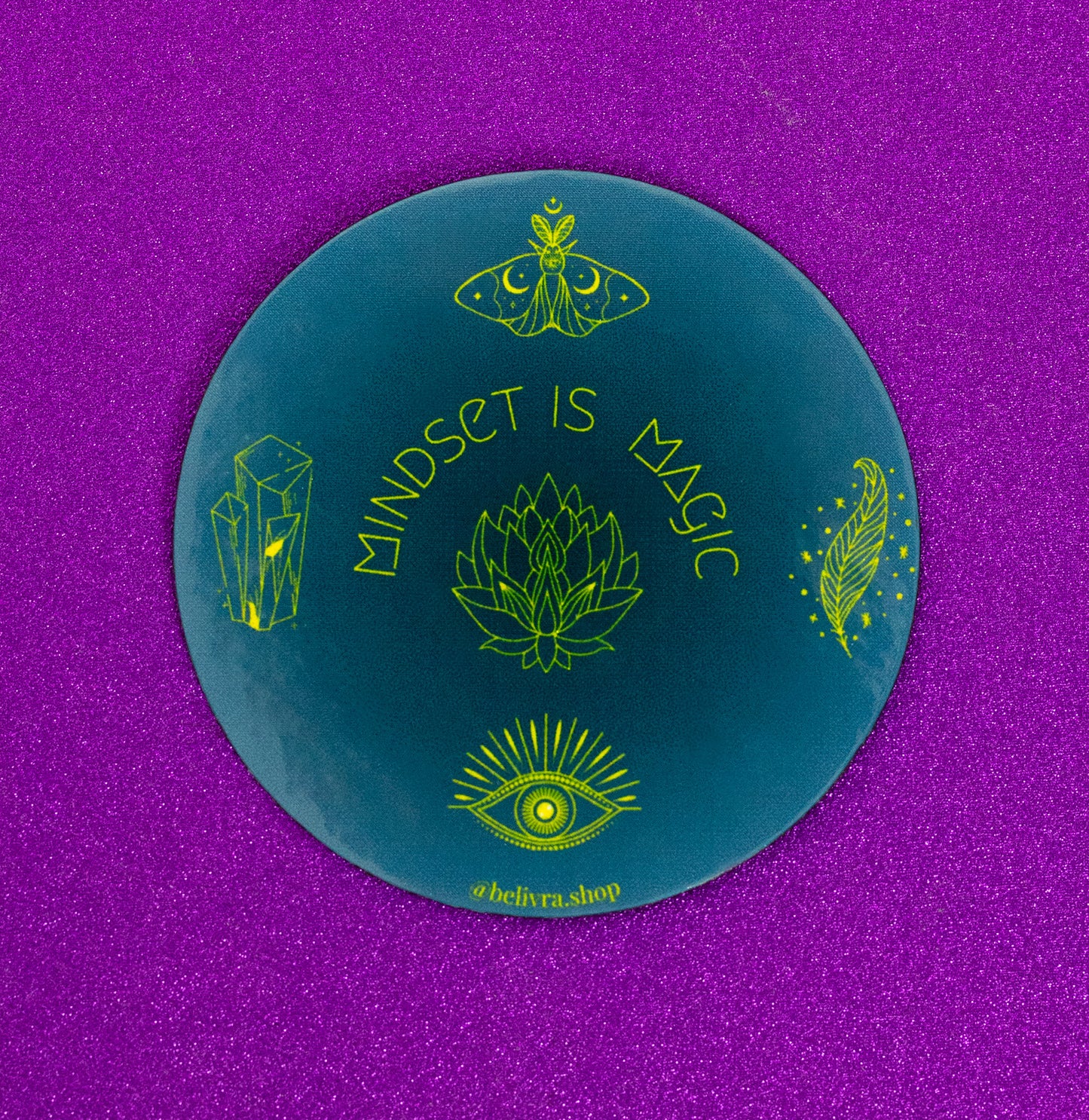 Belivra round motivational magnet with the affirmation "Mindset Is Magic" in bold yellow text – features mystical symbols including crystals, a lotus flower, moth, feather, and all-seeing eye on a deep blue background. Displayed on a sparkly purple surface, perfect for spiritual desk decor, fridge inspiration, or manifestation mindset tools.