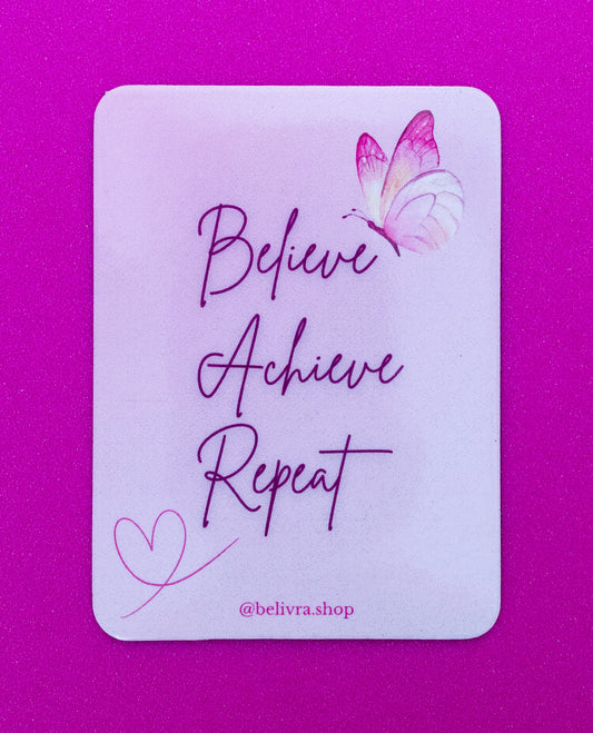 Belivra rectangular motivational magnet with the quote "Believe Achieve Repeat" in elegant script font – features a pink and purple butterfly and heart doodle on a soft pastel background. Displayed on a vibrant pink surface, perfect for empowering women’s workspaces, vision boards, or self-growth reminders.