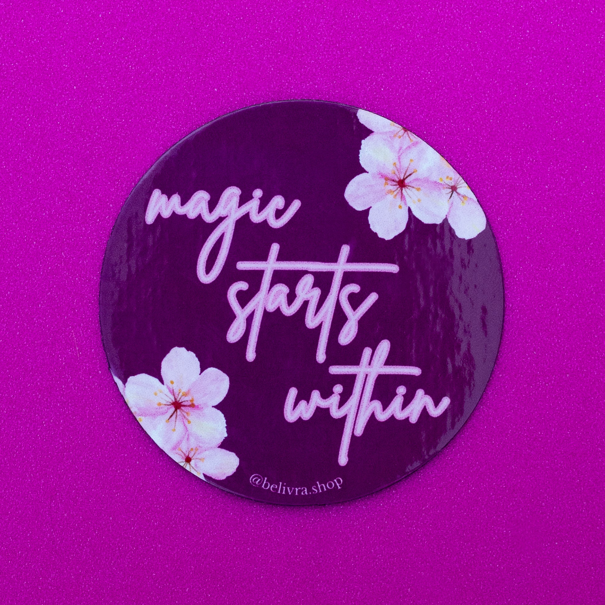 Belivra round inspirational magnet with the quote "magic starts within" in pink script font on a deep plum background – accented with delicate cherry blossom illustrations. Displayed on a vibrant pink surface, perfect for motivational home or office decor, fridge accessories, or empowering gifts for women.