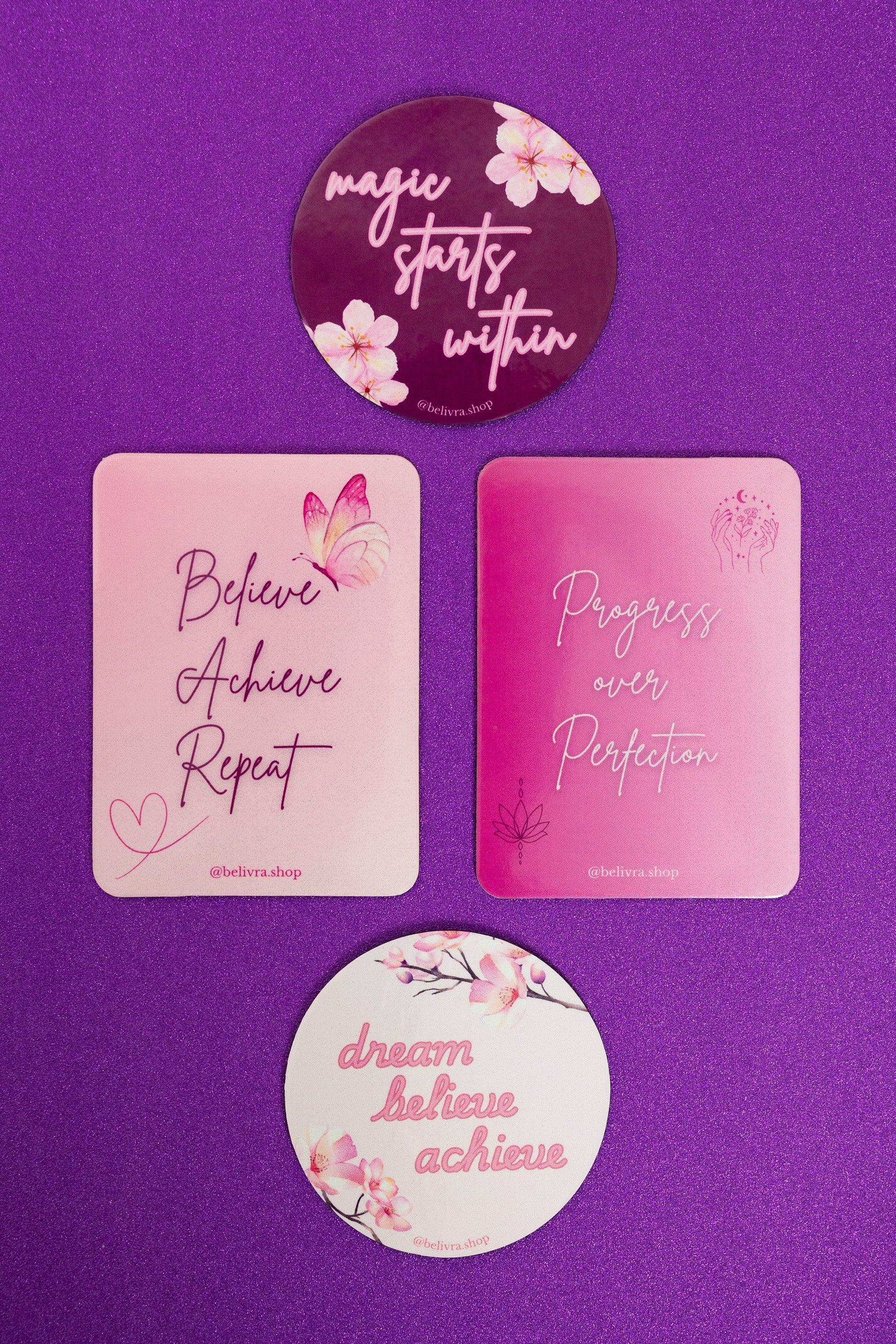 Set of 4 Belivra pink inspirational magnets displayed on a sparkly purple background – includes motivational quotes like "Believe Achieve Repeat," "Progress over Perfection," "Magic Starts Within," and "Dream Believe Achieve." Feminine aesthetic with floral and butterfly designs, perfect for fridge decor, vision boards, and empowering office or home spaces.
