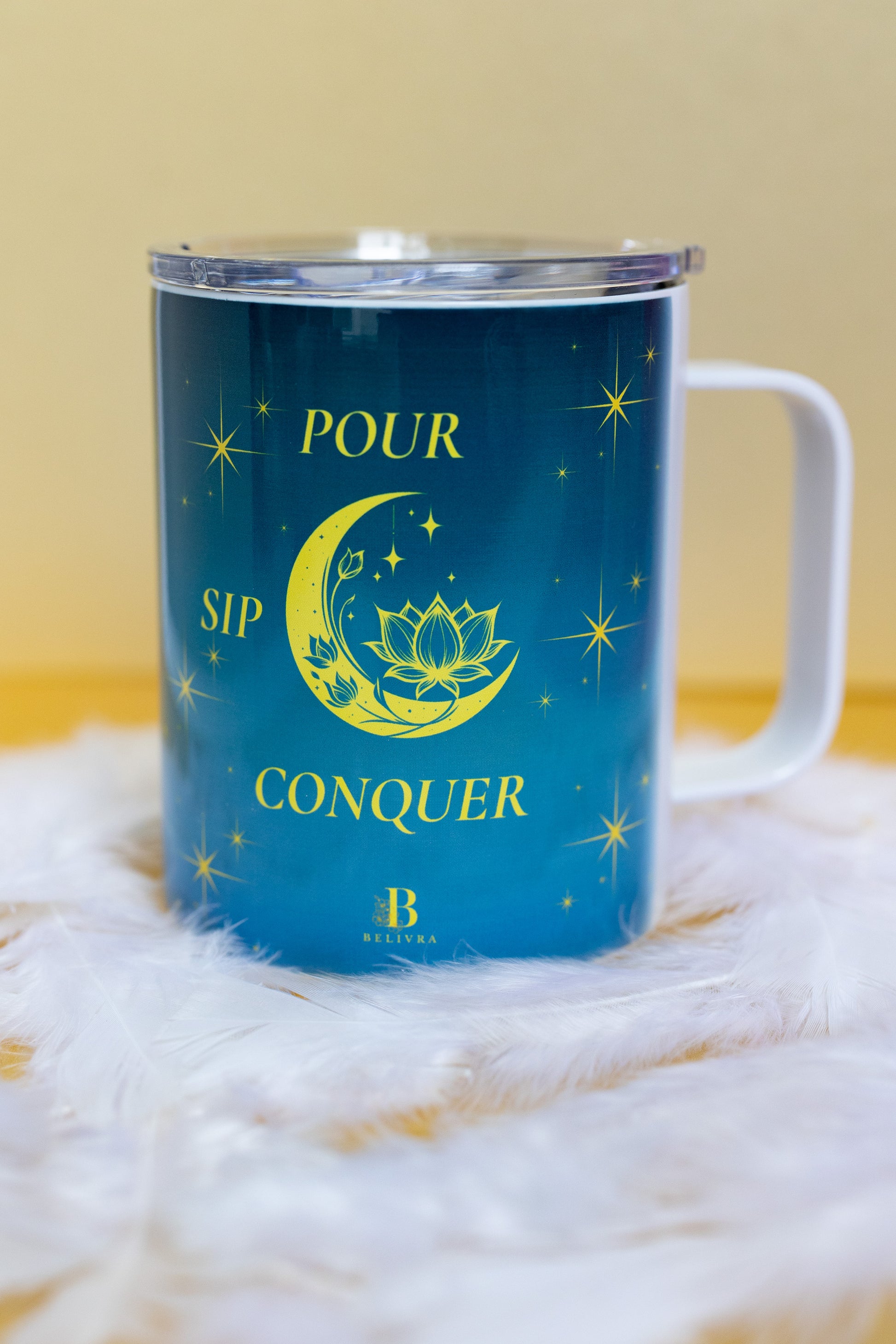 Front view of Belivra ceramic mug with a motivational quote "Pour. Sip. Conquer." in bold yellow text on a celestial blue background, featuring a crescent moon, lotus, and sparkling stars. Shown with a clear lid to keep beverages secure, perfect for mindful sipping and empowering morning routines. Ideal for tea, coffee, and gifting to women who embrace their journey with intention.