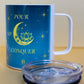 Angled view of Belivra ceramic mug with the quote "Pour. Sip. Conquer." in yellow text on a celestial blue background with a crescent moon, lotus, and stars. The mug is shown with a clear lid, ideal for maintaining the temperature of your favorite beverages. A perfect accessory for empowered morning rituals, mindful sipping, and cozy desk moments.