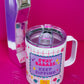Top-down view of Belivra insulated tumbler mug with clear spill-resistant lid and bold quote "Stay Badass. Keep Sipping." in vibrant pink and purple lettering. Features a fun red grid design with colorful icons like diamonds, flowers, and stars. Styled on a hot pink surface with a retro phone and scattered paperclips, ideal for empowering coffee moments and stylish desk vibes.