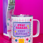 Front view of Belivra insulated tumbler mug with clear lid and bold affirmation "Stay Badass. Keep Sipping." in pink and purple text – set against a playful red grid background with doodles like flowers, diamonds, and stars. Displayed with a retro phone and scattered paperclips on a hot pink surface, this travel-friendly mug is perfect for empowering coffee or tea moments at home, work, or on the go.