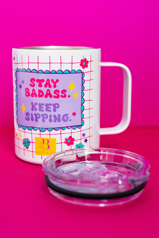 Belivra insulated tumbler mug with motivational quote "Stay Badass. Keep Sipping." in bold pink and purple text – shown with removable clear lid and a playful pink grid background featuring floral and diamond doodles. Perfect for hot or cold drinks, this stylish and empowering travel mug is ideal for busy women, entrepreneurs, and coffee lovers on the go.