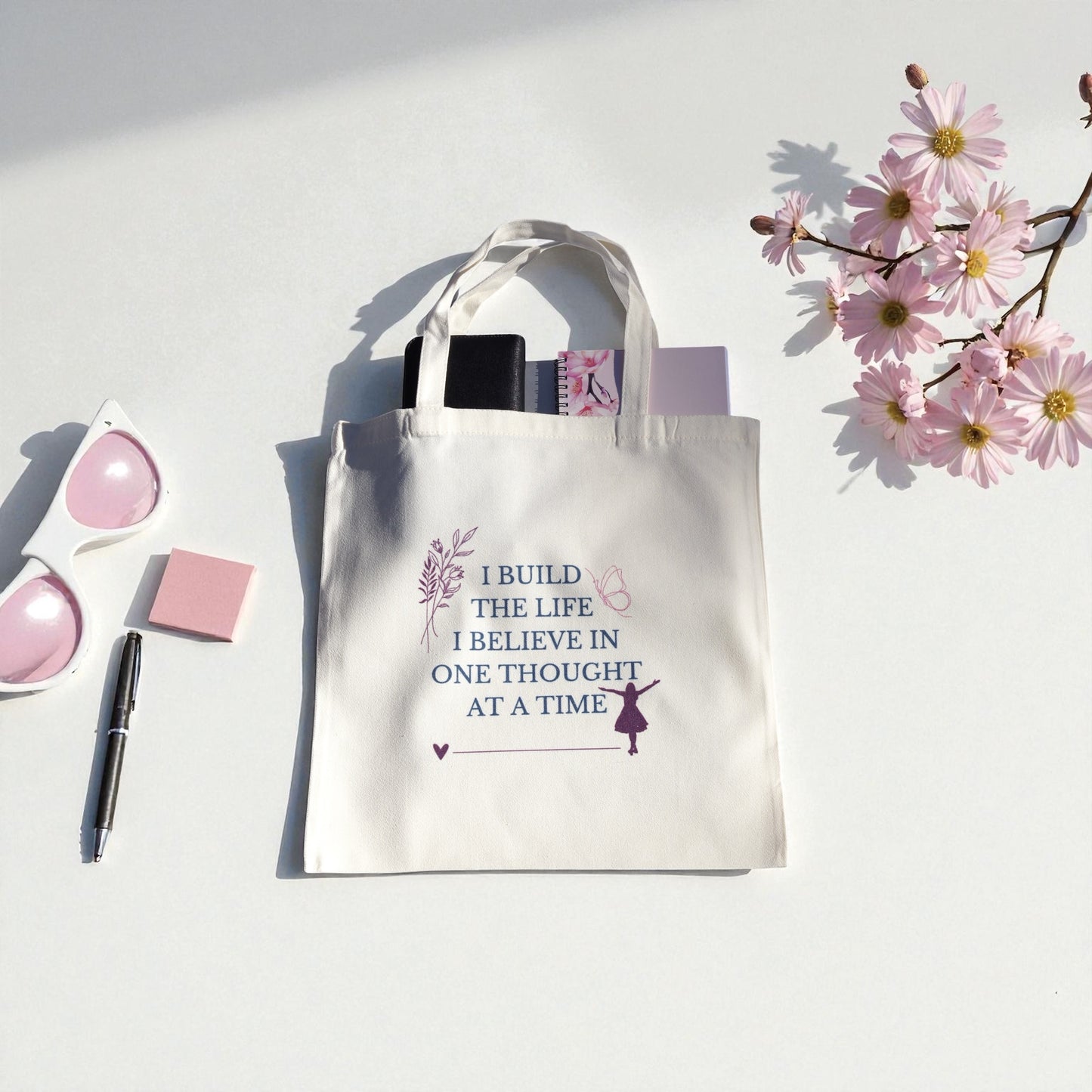 Cream-colored tote bag with the quote “I Build the Life I Believe In, One Thought at a Time” in teal and plum text, symbolizing mindfulness and intentional living.