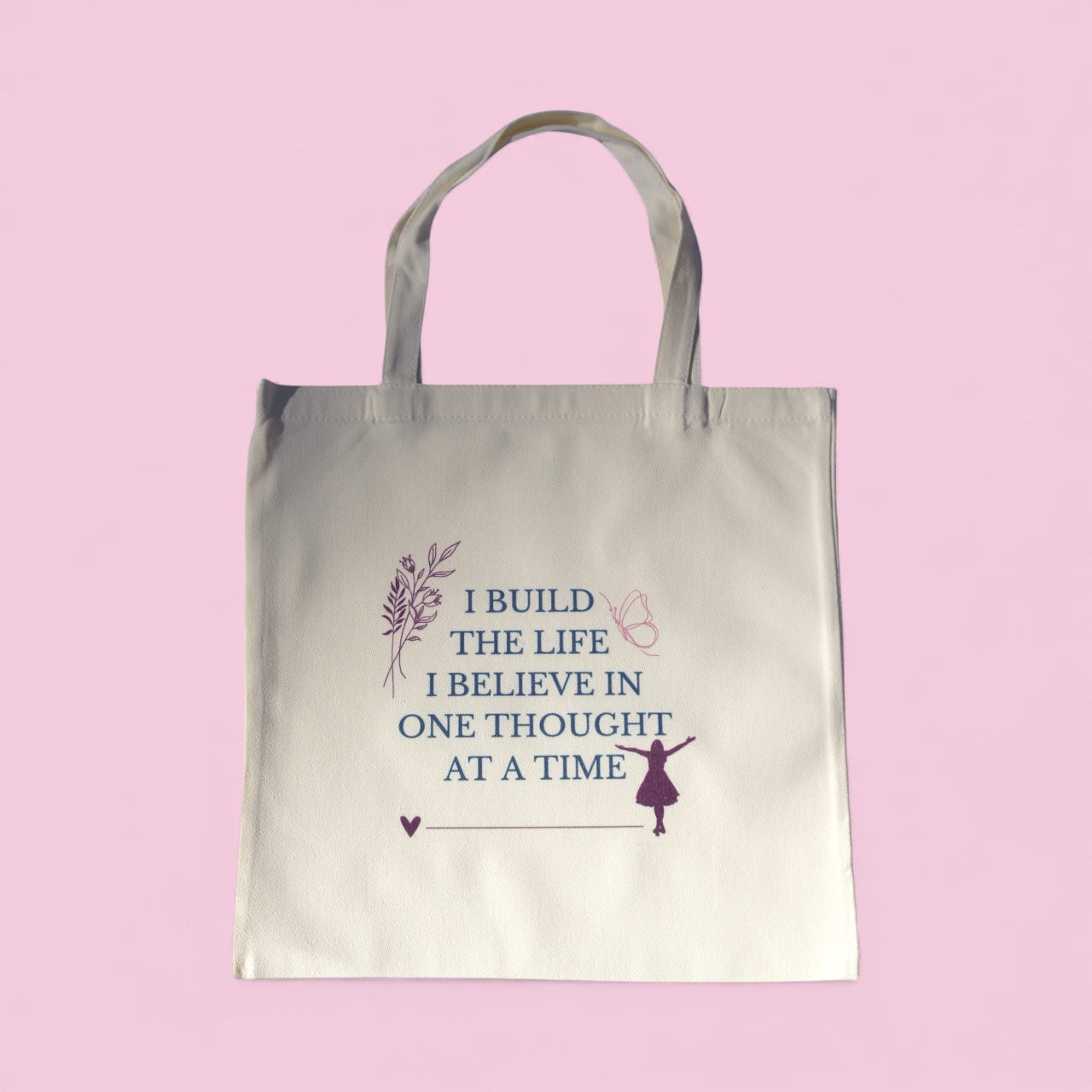 Cream-colored tote bag with the quote “I Build the Life I Believe In, One Thought at a Time” in teal and plum text, symbolizing mindfulness and intentional living.
