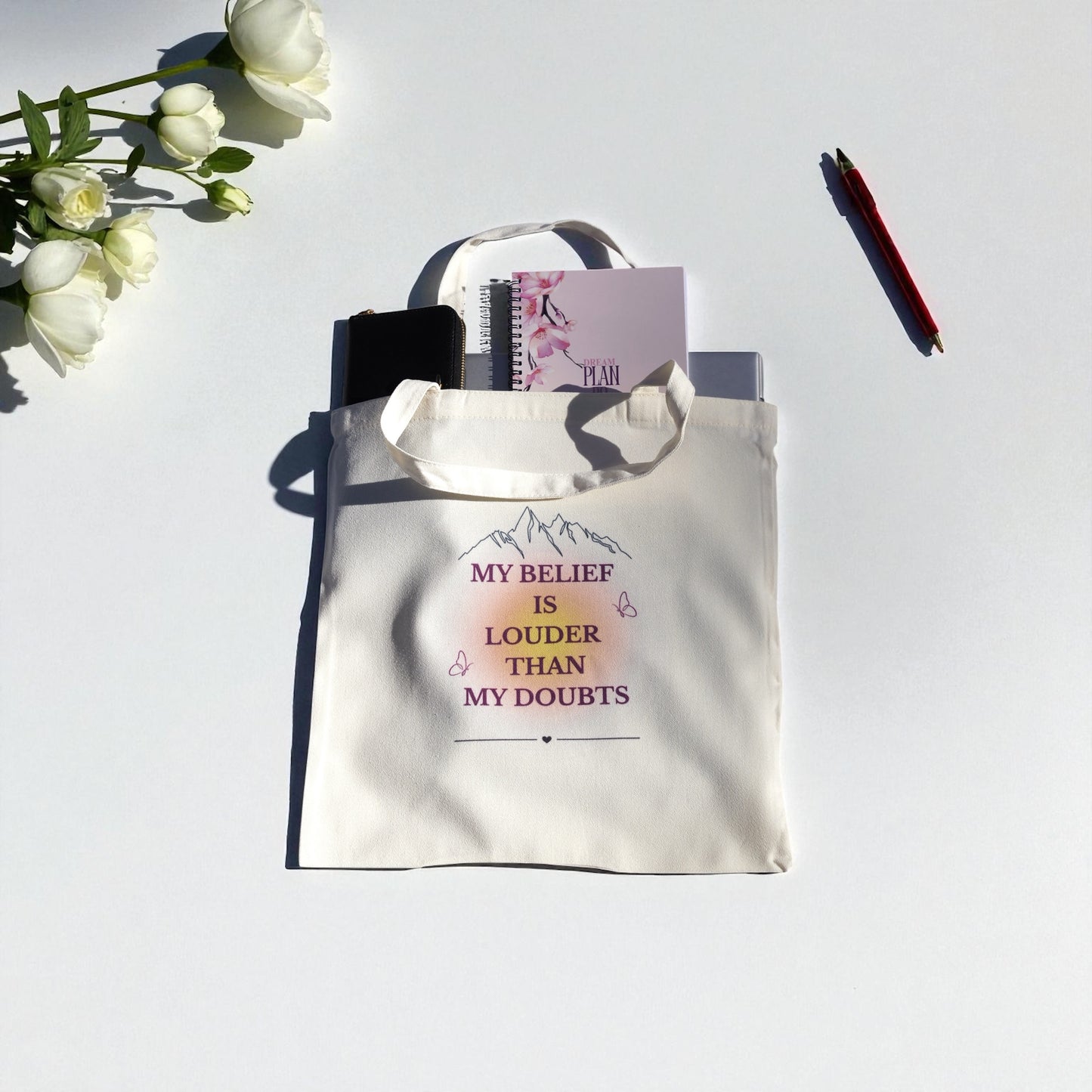 Cream tote bag with the quote “My Belief Is Louder Than My Doubts” in plum and gold text, featuring minimalist mountain and butterfly design symbolizing confidence and growth.