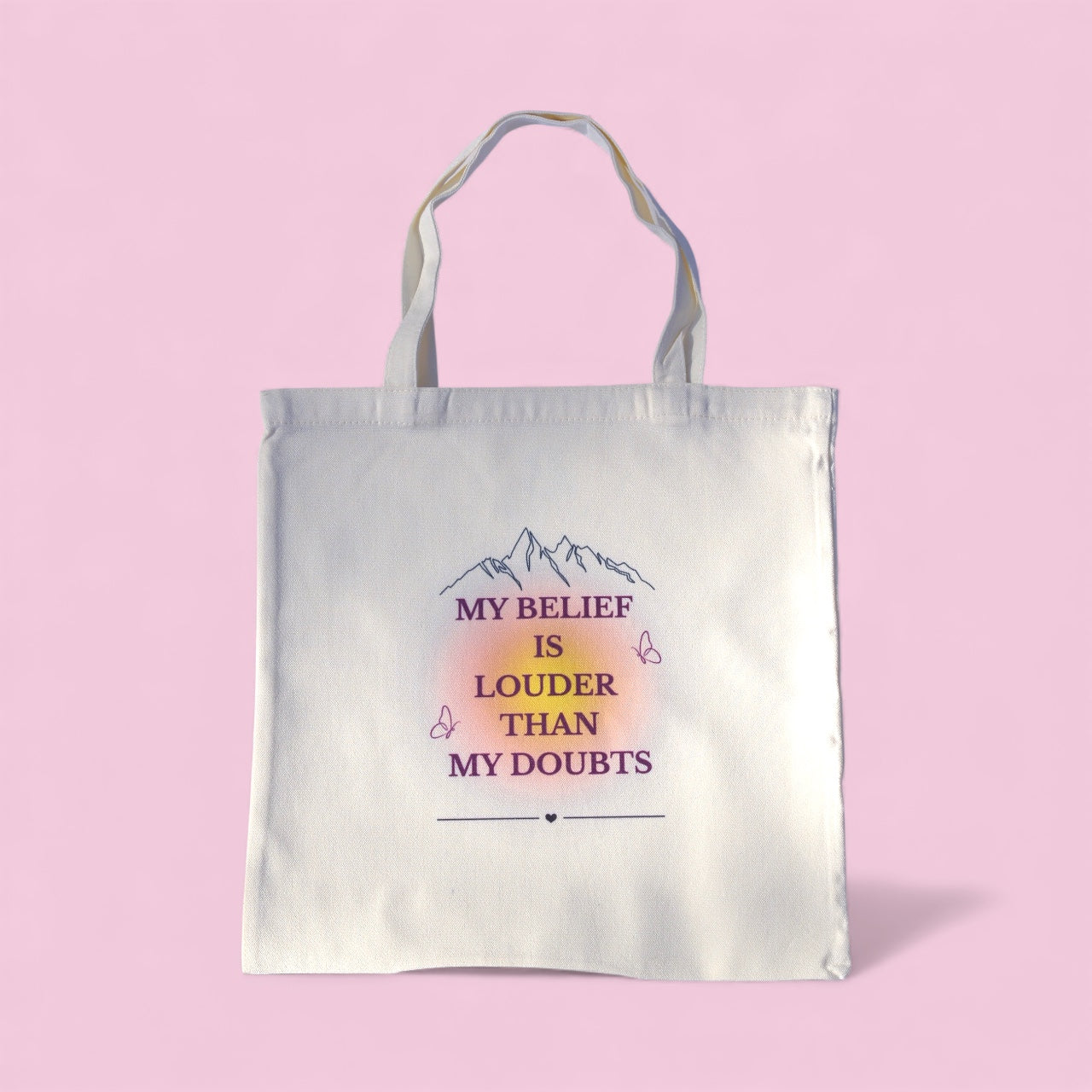 Cream tote bag with the quote “My Belief Is Louder Than My Doubts” in plum and gold text, featuring minimalist mountain and butterfly design symbolizing confidence and growth.