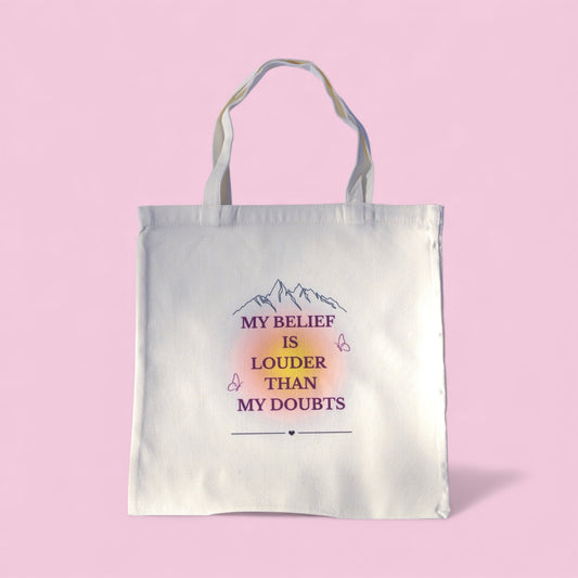 Cream tote bag with the quote “My Belief Is Louder Than My Doubts” in plum and gold text, featuring minimalist mountain and butterfly design symbolizing confidence and growth.