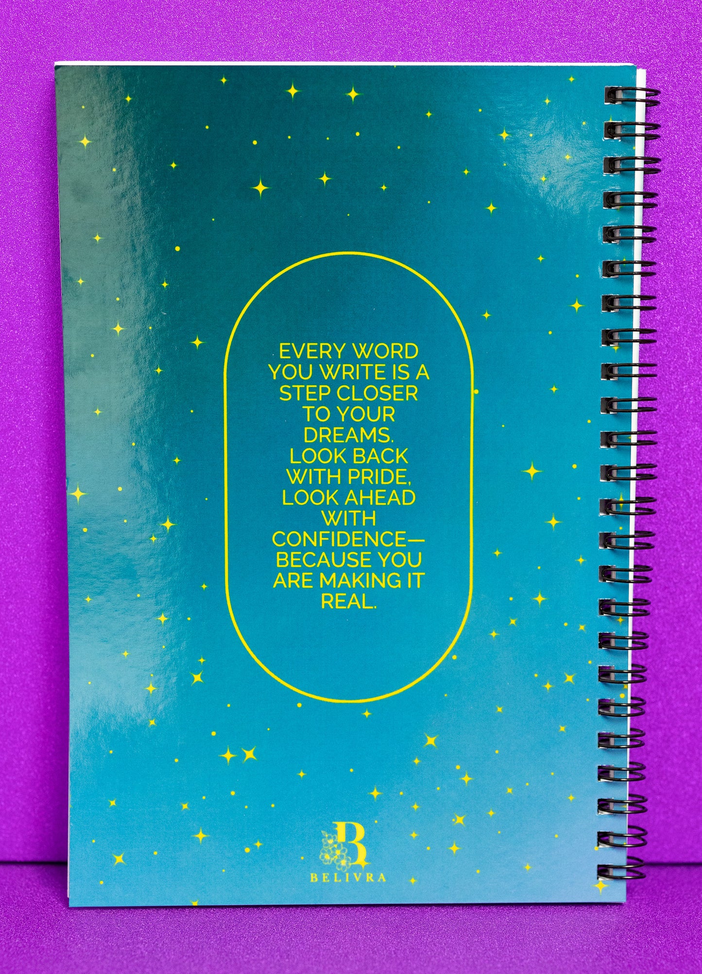 A spiral-bound notebook by Belivra, showcasing a captivating teal cover with gold stars and the inspirational quote: "Every word you write is a step closer to your dreams. Look back with pride, look ahead with confidence—because you are making it real." This motivational notebook is perfect for journaling, goal-setting, and affirmations, encouraging progress toward personal and professional goals.