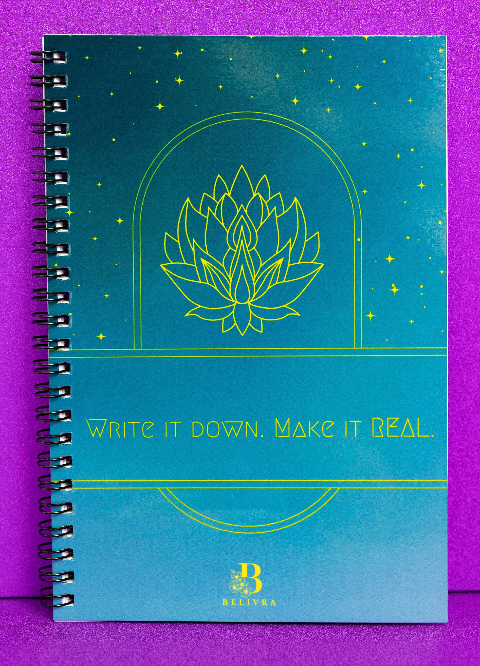A spiral-bound notebook from Belivra, featuring an elegant teal cover with a gold lotus design and the empowering phrase "Write It Down. Make It Real." The notebook serves as a tool for capturing dreams, goals, and affirmations, inspiring action and manifestation. Perfect for those looking to write and achieve their vision. Ideal for planners, visionaries, and creatives.