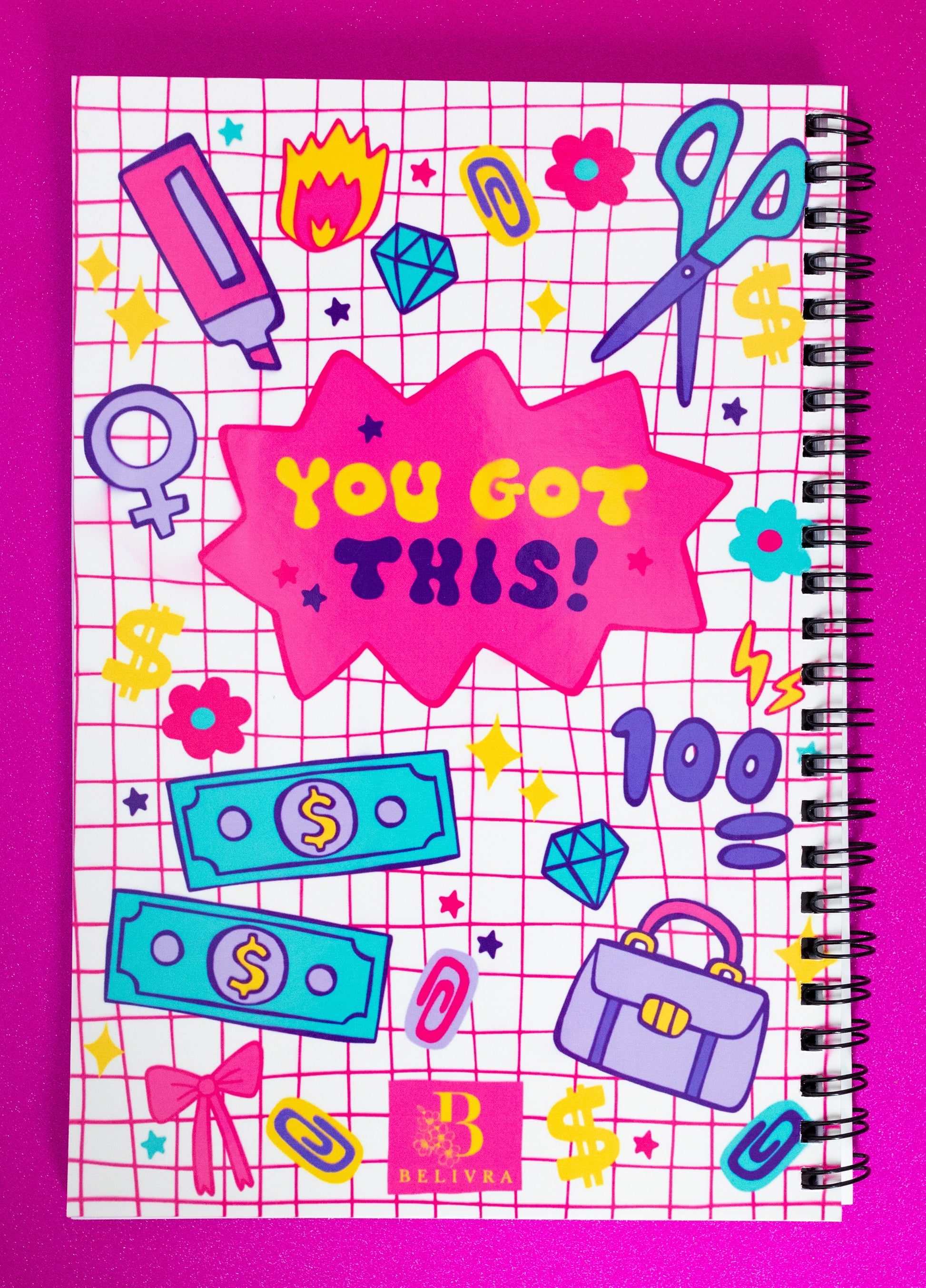 Back of Belivra spiral notebook featuring the motivational phrase "You Got This!" in bold lettering on a pink starburst – surrounded by playful doodles like scissors, money, a briefcase, diamonds, and female empowerment symbols. Displayed on a glittery pink background, this vibrant notebook is perfect for goal setting, journaling, or creative planning for ambitious women and students.