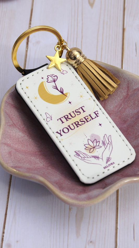 Trust Yourself keychain by Belivra with gold moon, star charm and tassel on pink ceramic dish
